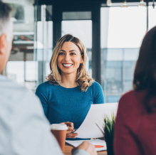Woman in a blue sweater sitting at a table in a meeting facing two other people